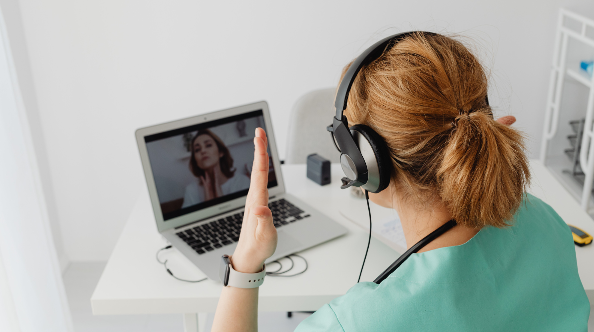 Female healthcare worker wearing a headset during a virtual video consultation on a laptop.