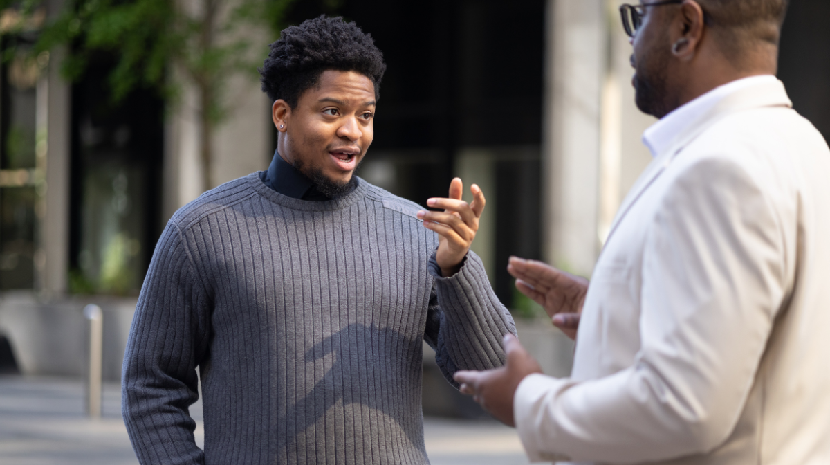 Two professionals conversing outdoors, one animatedly explaining while the other listens and gestures.