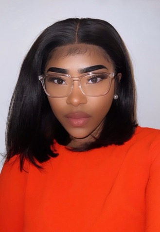 Young adult woman wearing clear glasses and an orange top, facing camera with a neutral expression.