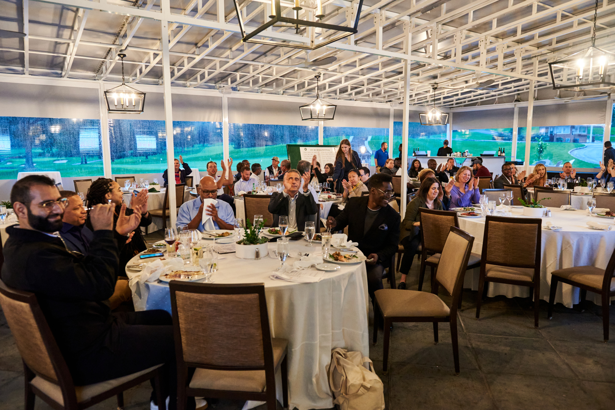 Attendees at a seated dinner event listening and applauding.