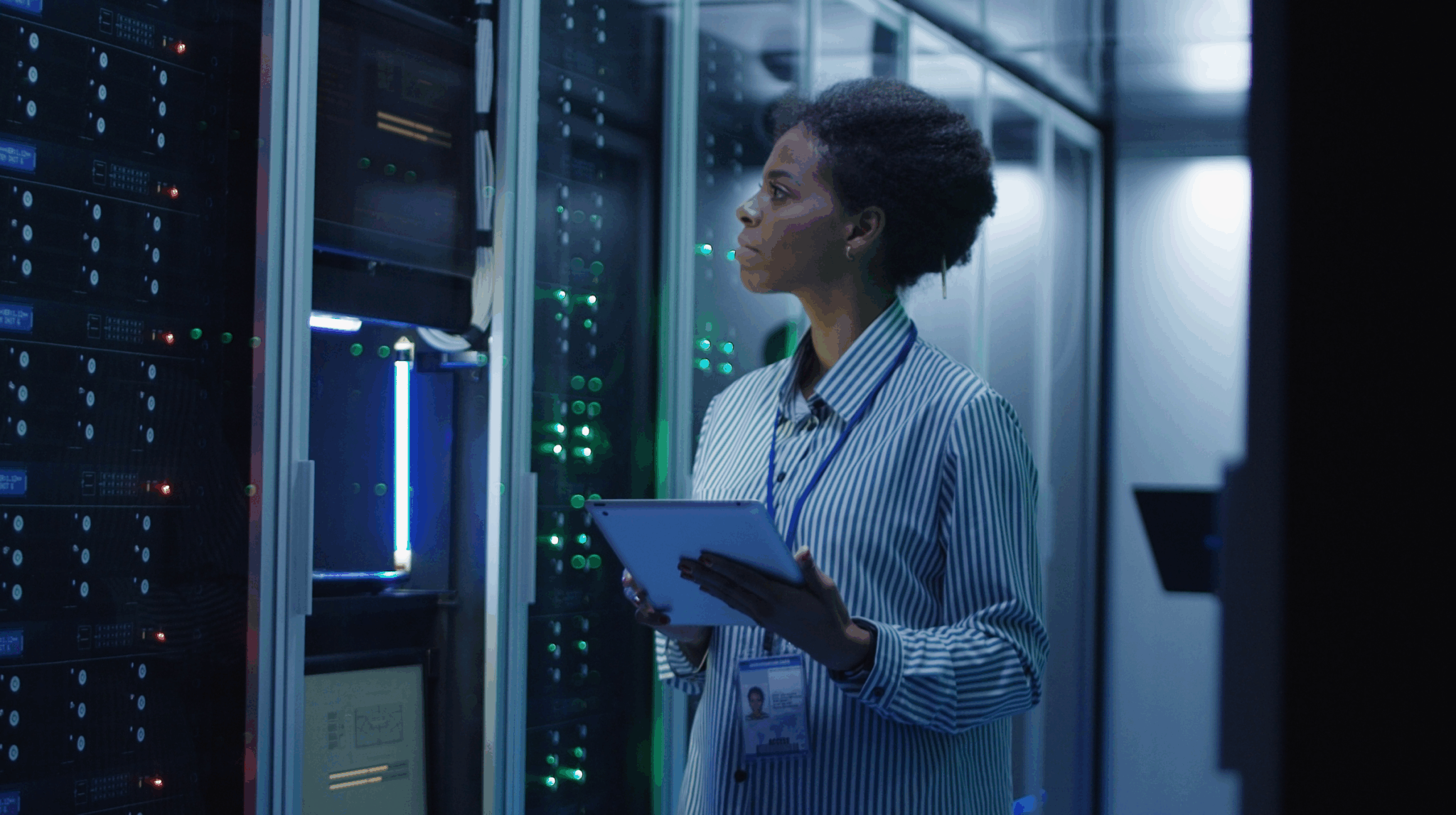 Female technician inspecting servers in a data center while holding a tablet.