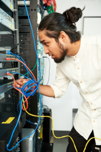 Young adult leaning into a server rack, connecting network cables to equipment.