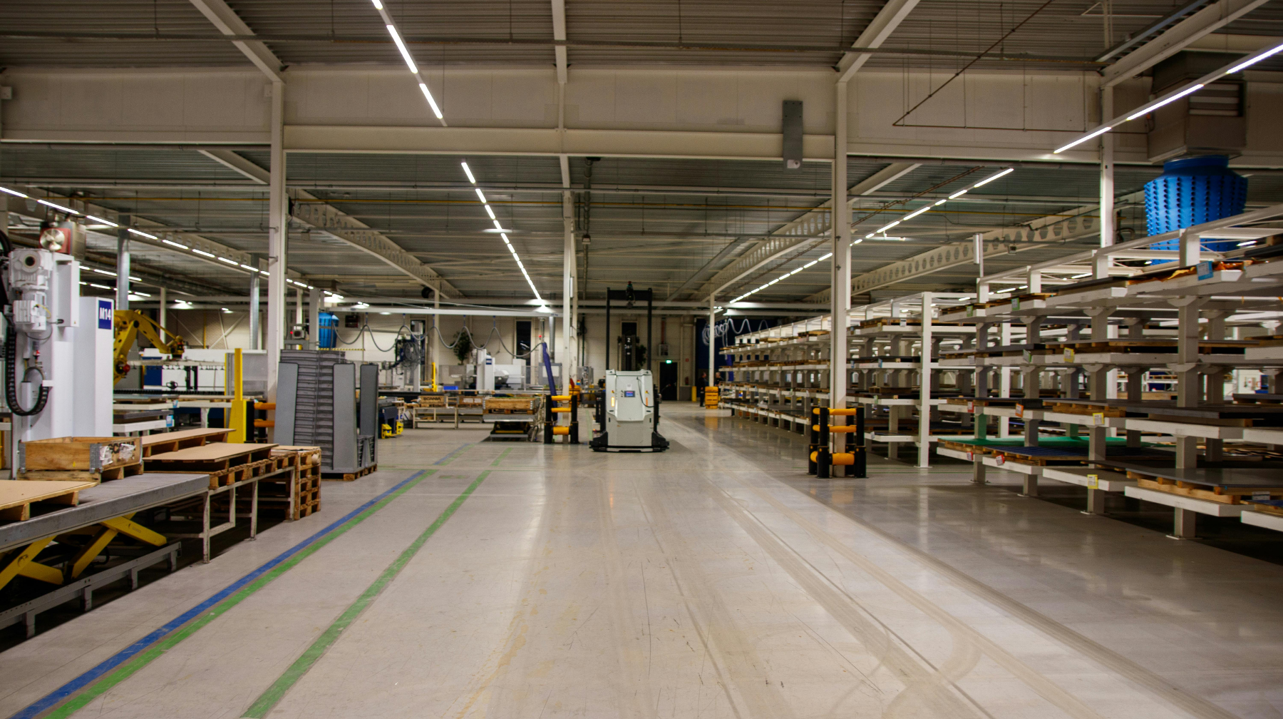 Large empty industrial workshop with wide aisle, shelving and workstations on either side and equipment parked in the center.