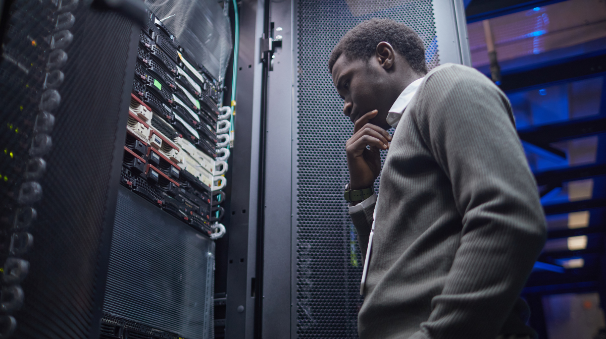 Man standing in a server room examining a rack of servers.