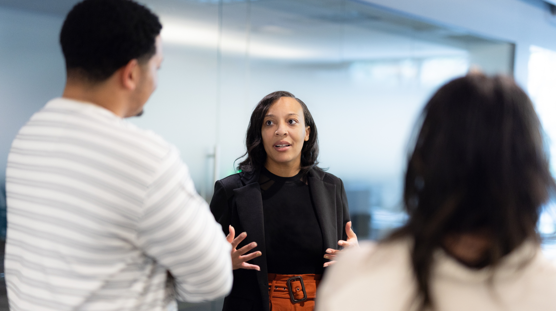 Woman speaking and gesturing to two colleagues in a workplace conversation.