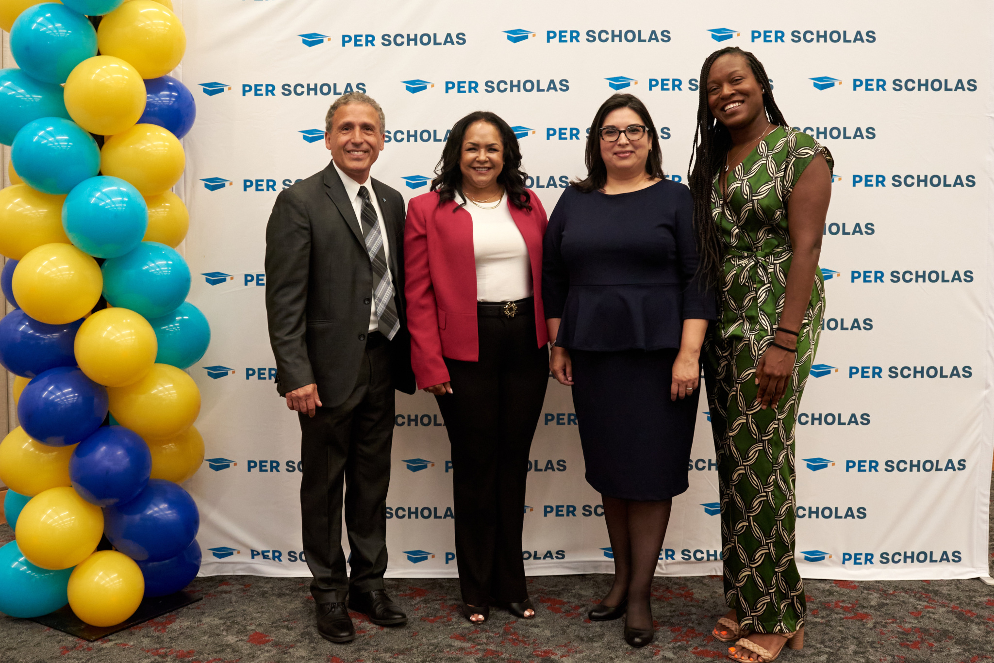 Four adults standing and smiling in front of a Per Scholas step-and-repeat backdrop at an event.