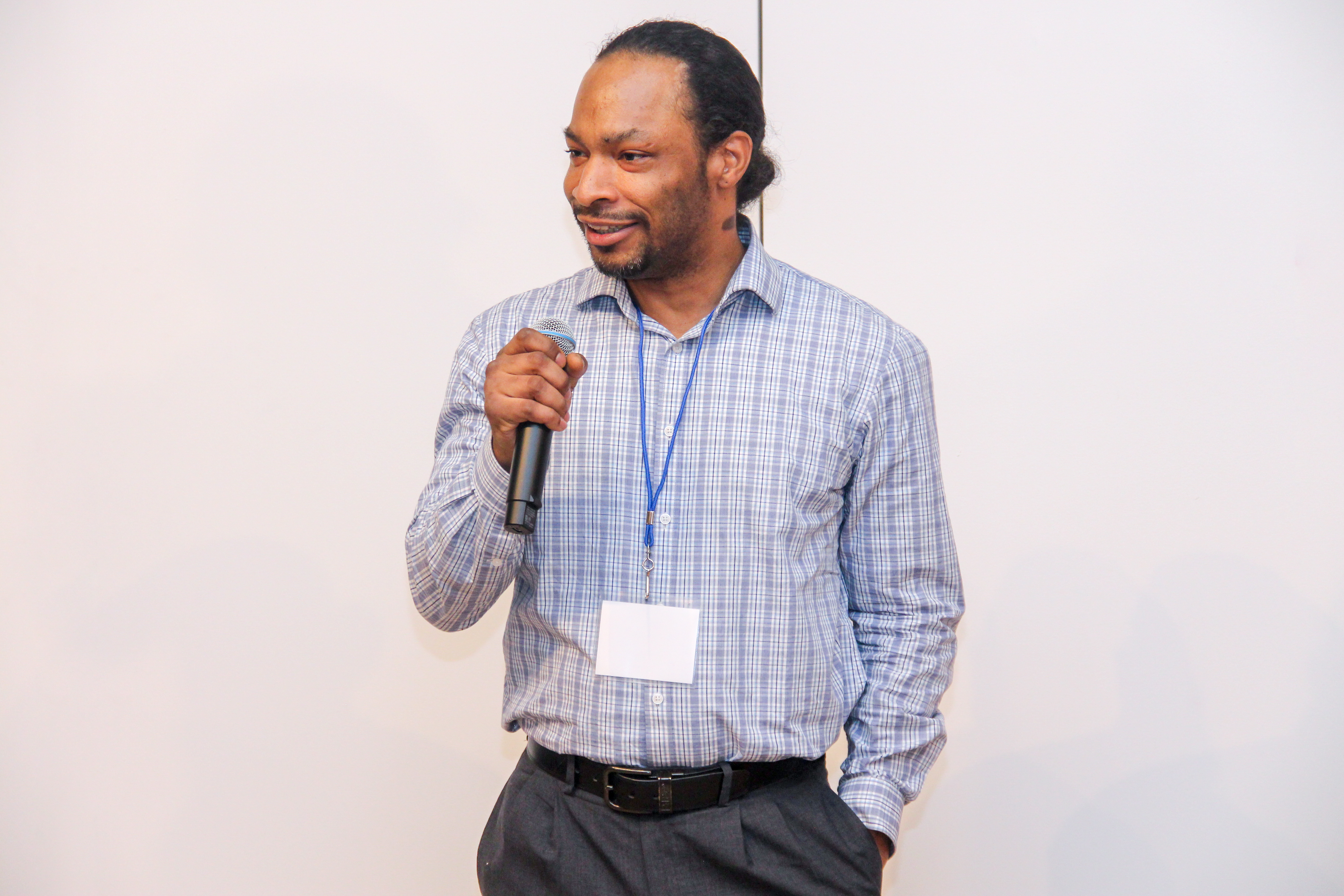 Man speaking into a microphone at an event, wearing a name badge.