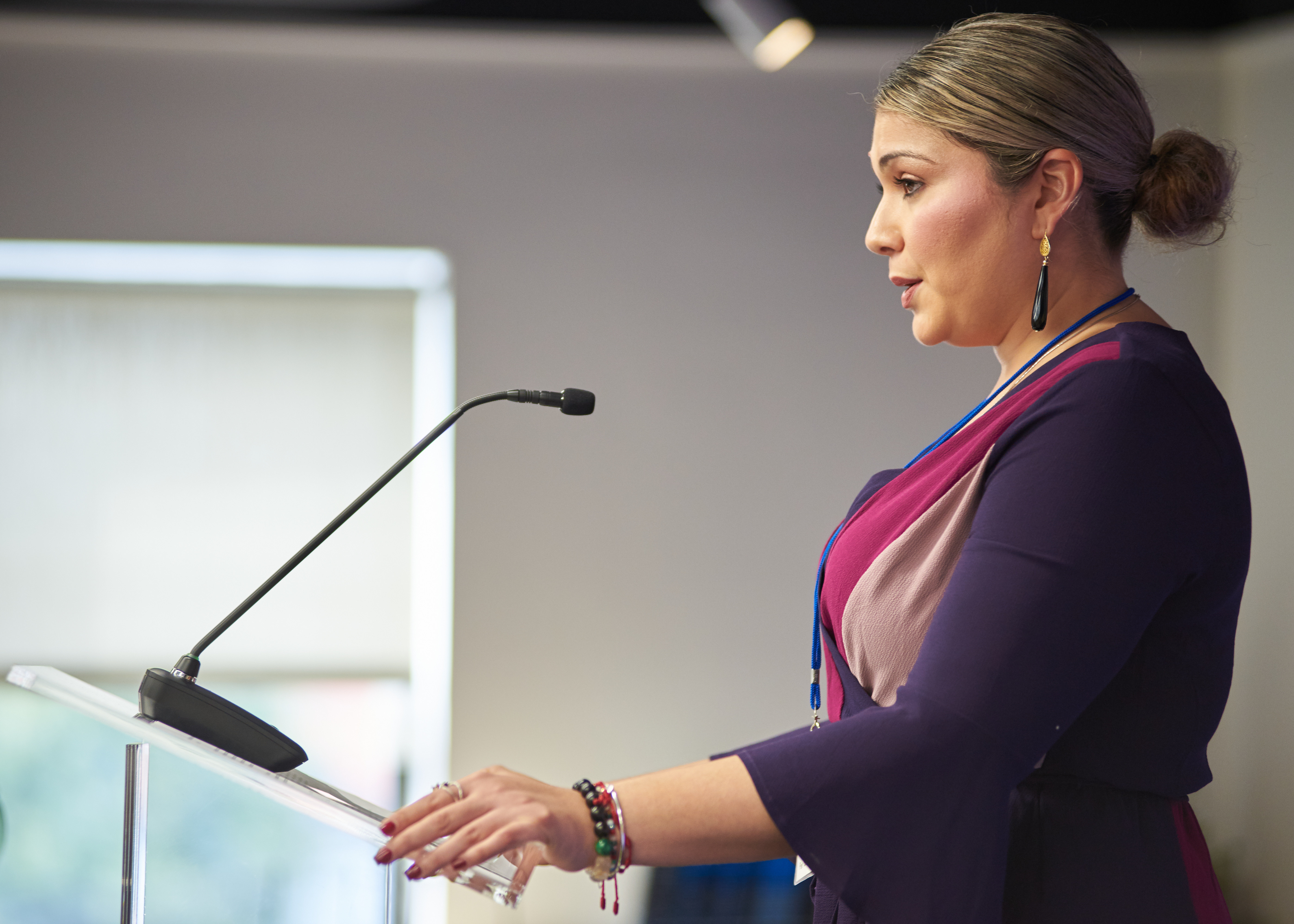 Woman speaking at a podium with a microphone, addressing an audience.