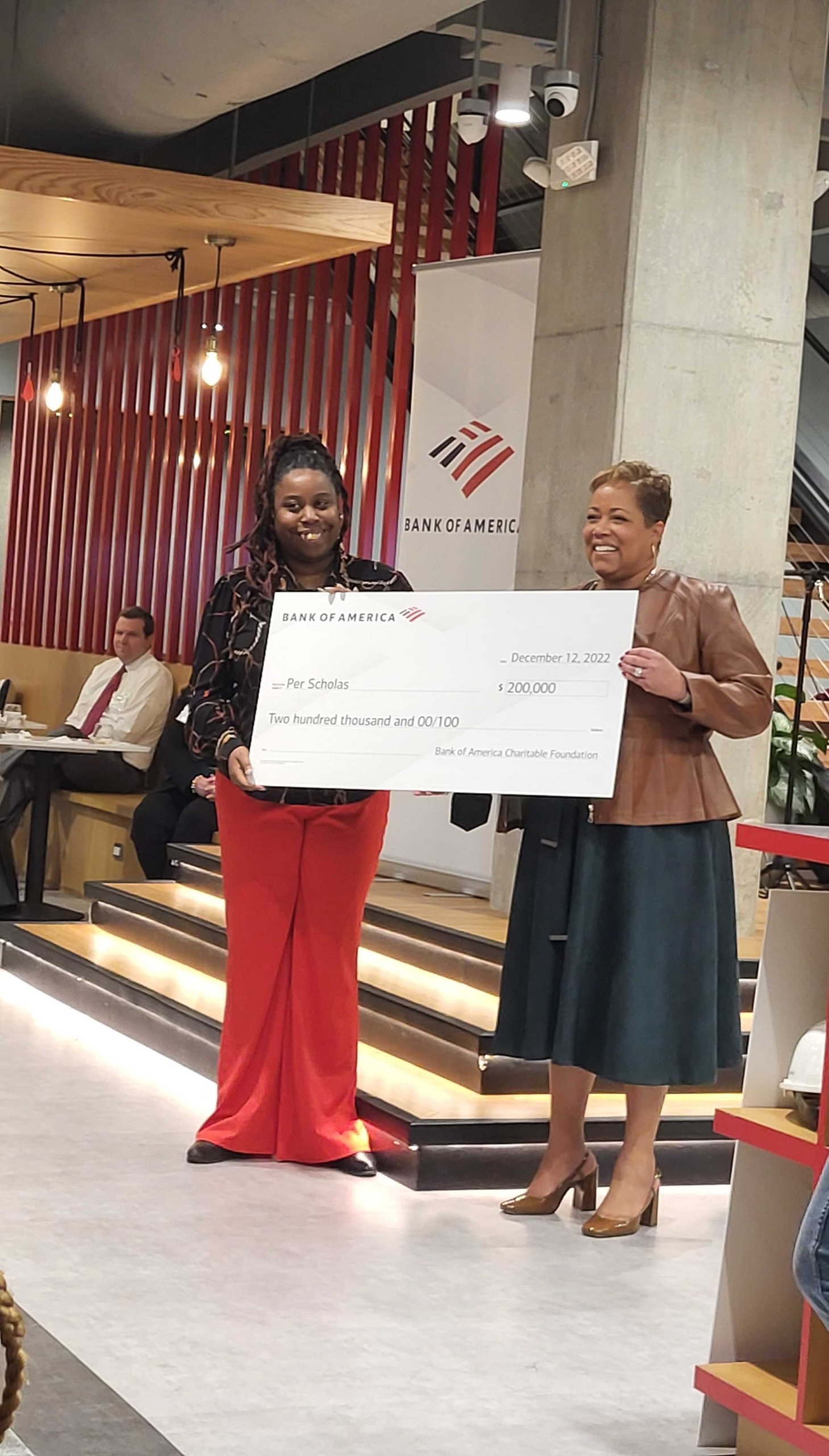 Two smiling women hold a large ceremonial check from Bank of America for $200,000 made out to Per Scholas.
