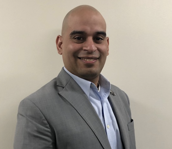 Headshot of Hugo Canedo smiling in a suit against a plain wall.