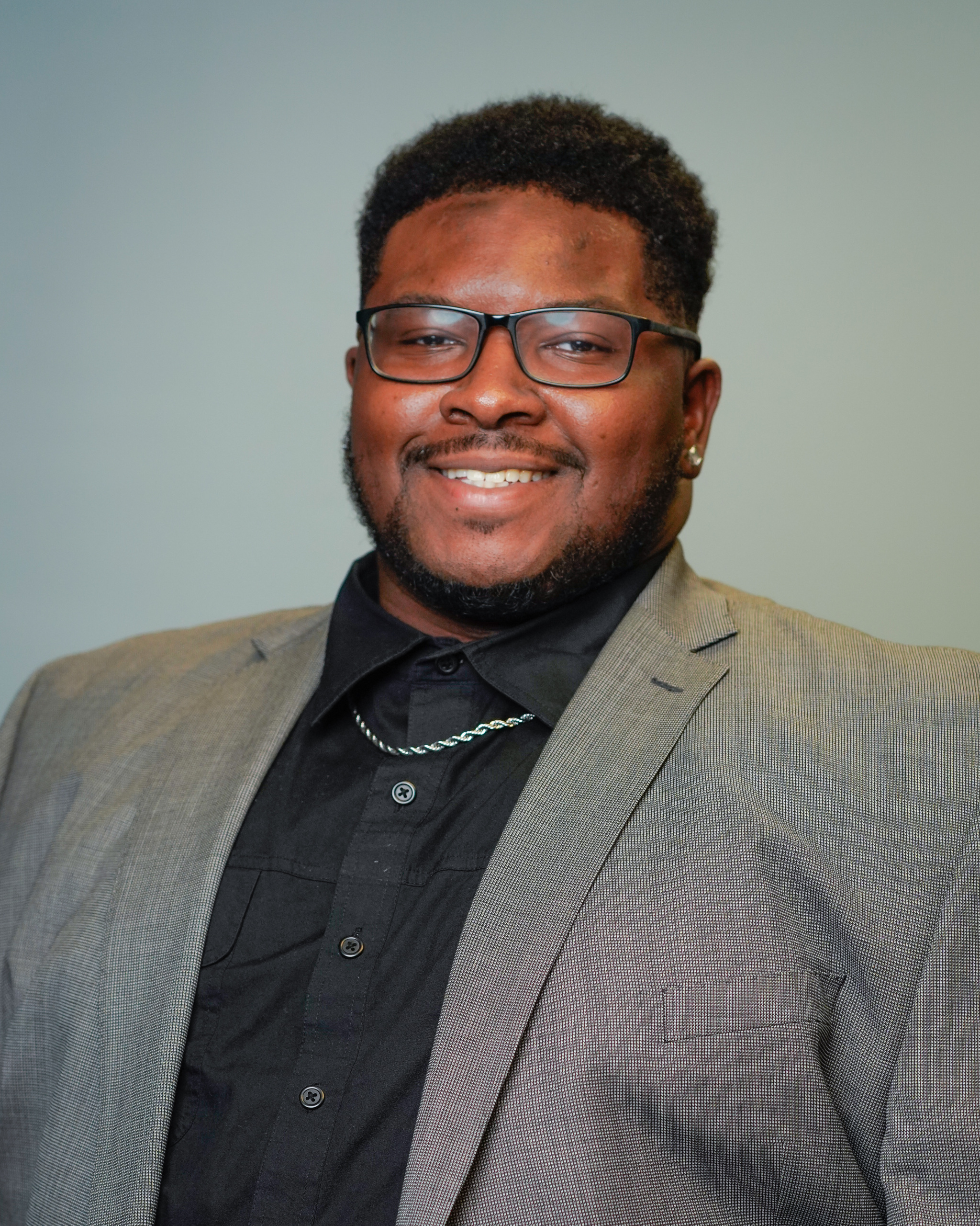 Headshot of a man in a suit jacket and glasses.