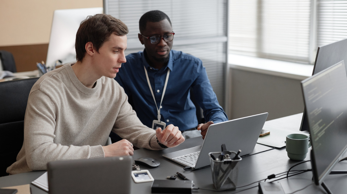 Experienced cybersecurity professional mentoring a junior colleague at a desk in an office