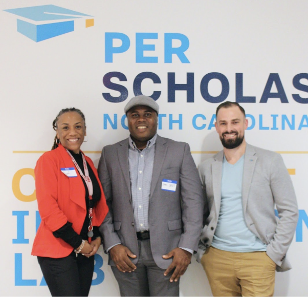 Three smiling adults standing in front of a Per Scholas North Carolina wall.