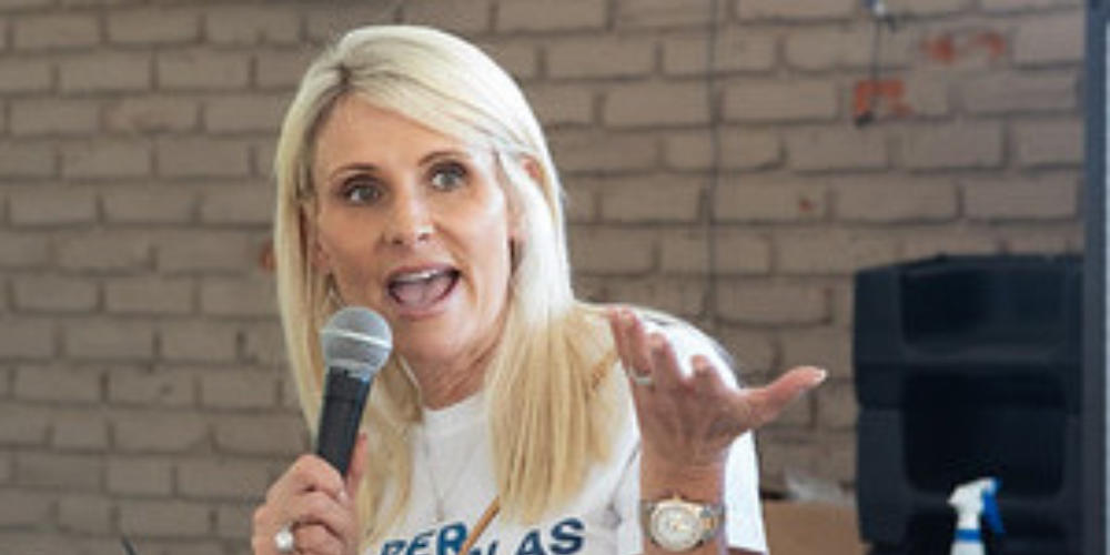 Woman speaking into a microphone while gesturing, addressing an audience.