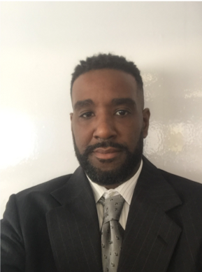 Head-and-shoulders portrait of a man in a suit and tie facing the camera with a neutral expression.