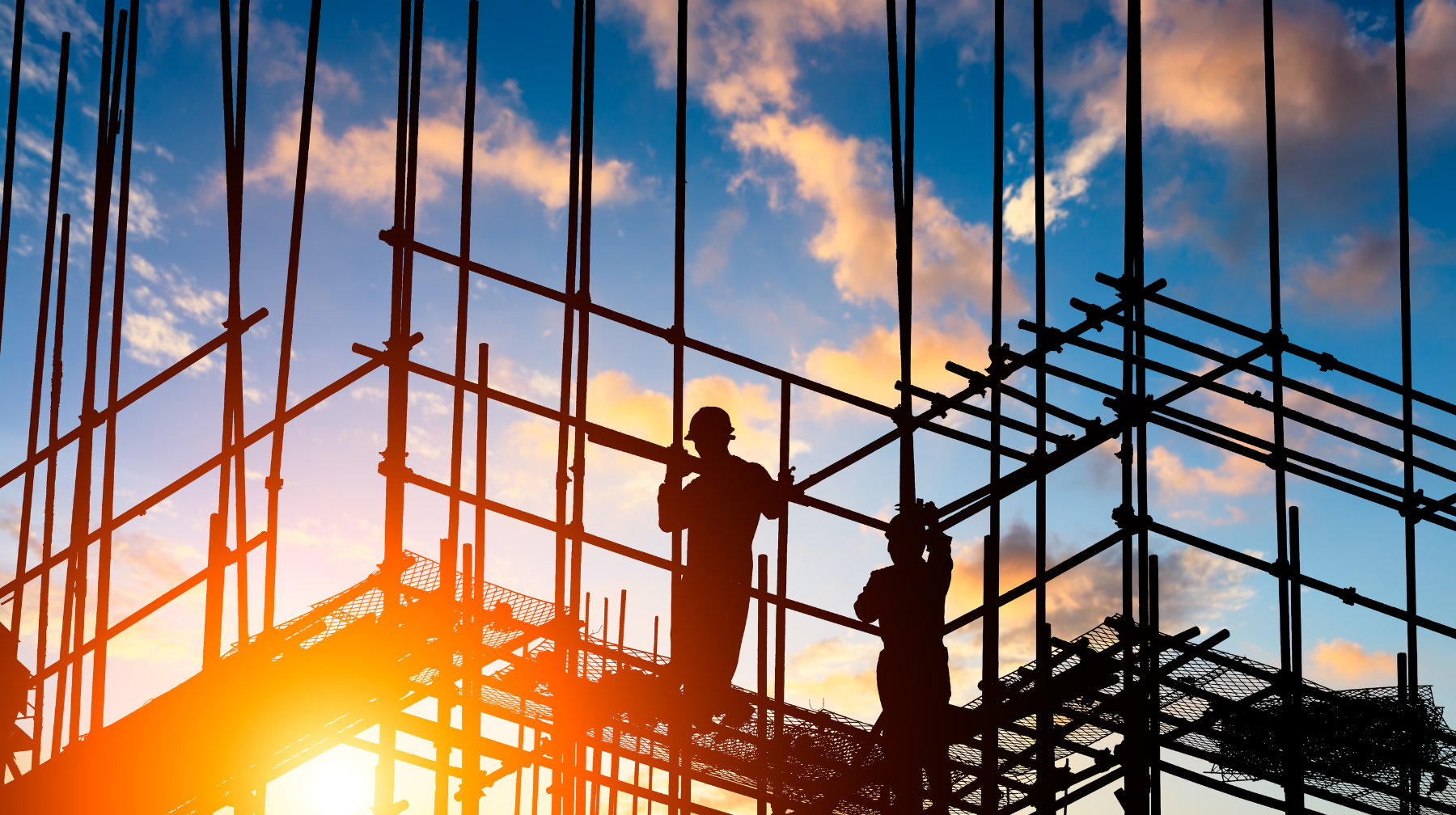 Silhouetted construction workers assembling scaffolding at a building site during sunrise.