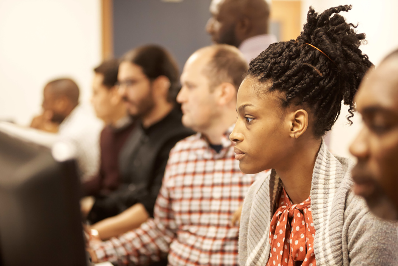 Male and female learners seated in a classroom working at computers, focused on instruction.