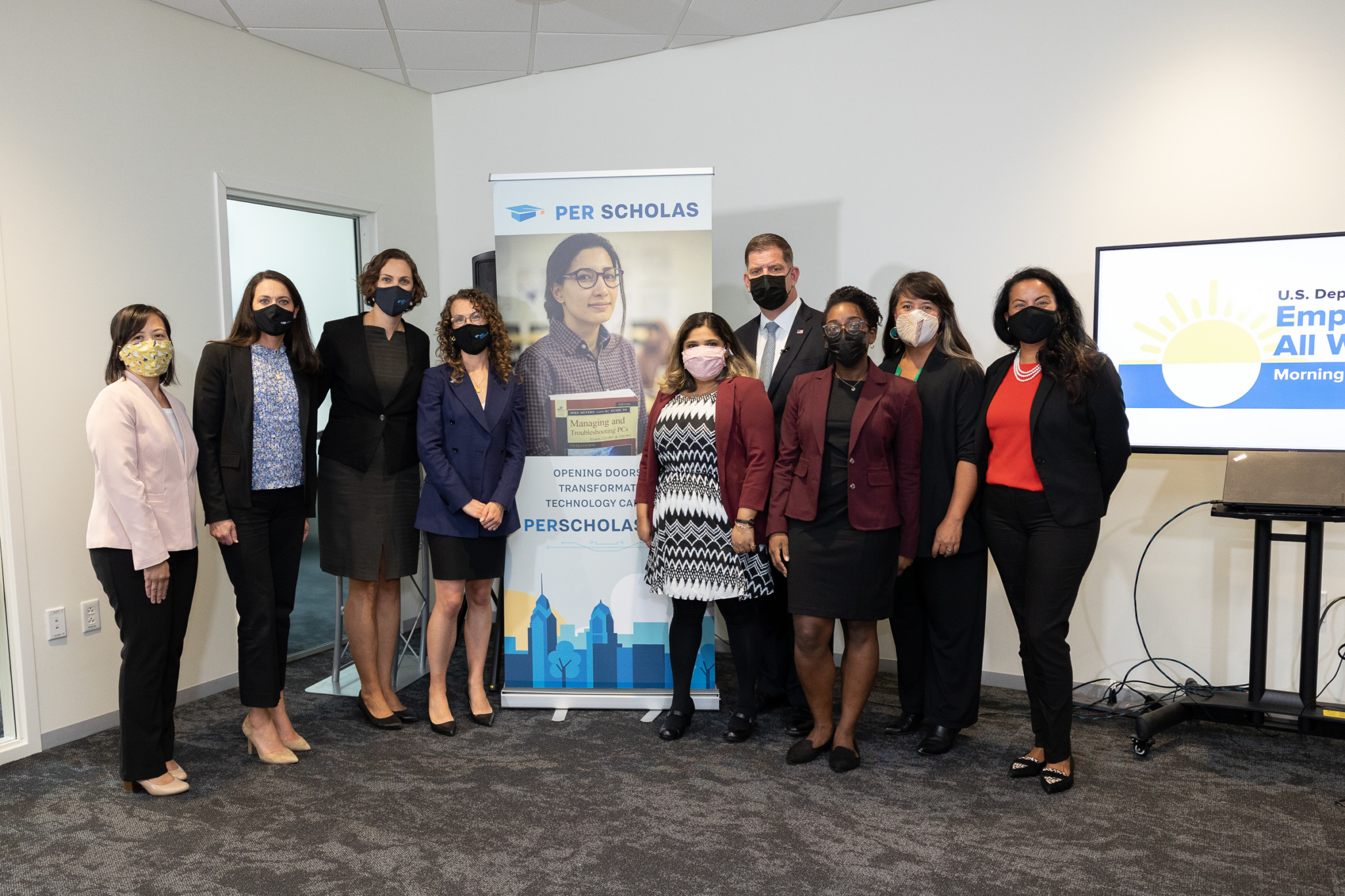 Group of masked adults standing together in an office beside a Per Scholas banner.