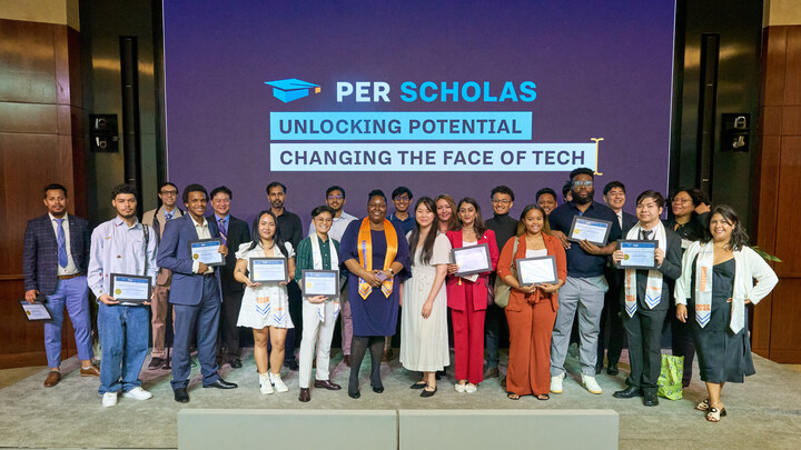 Per Scholas graduates standing on stage holding certificates beneath a screen that reads "Per Scholas Unlocking Potential Changing the Face of Tech."