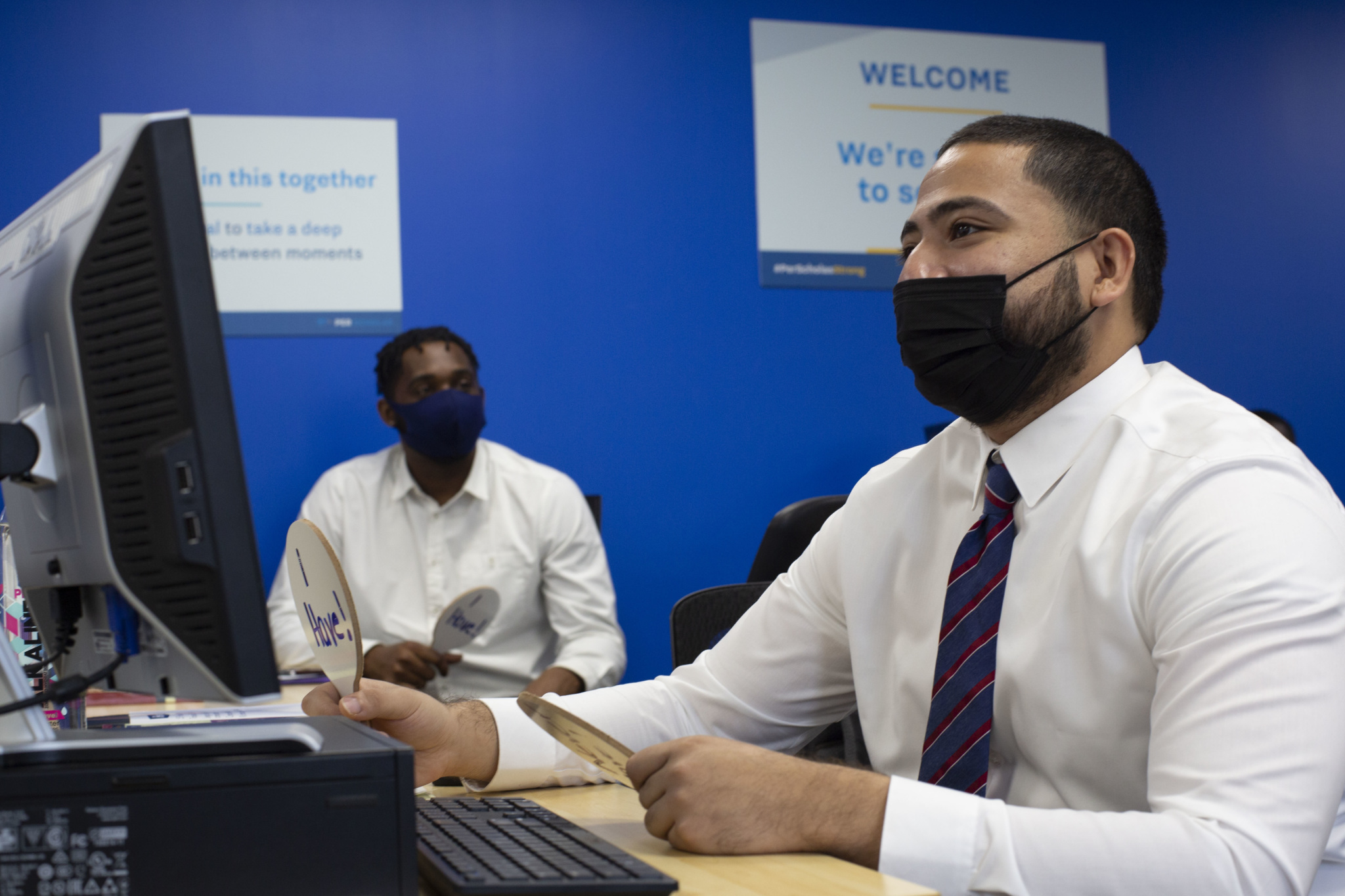 Two adult learners wearing masks sit at computers in a classroom, while holding paddles during an instructor-led activity.