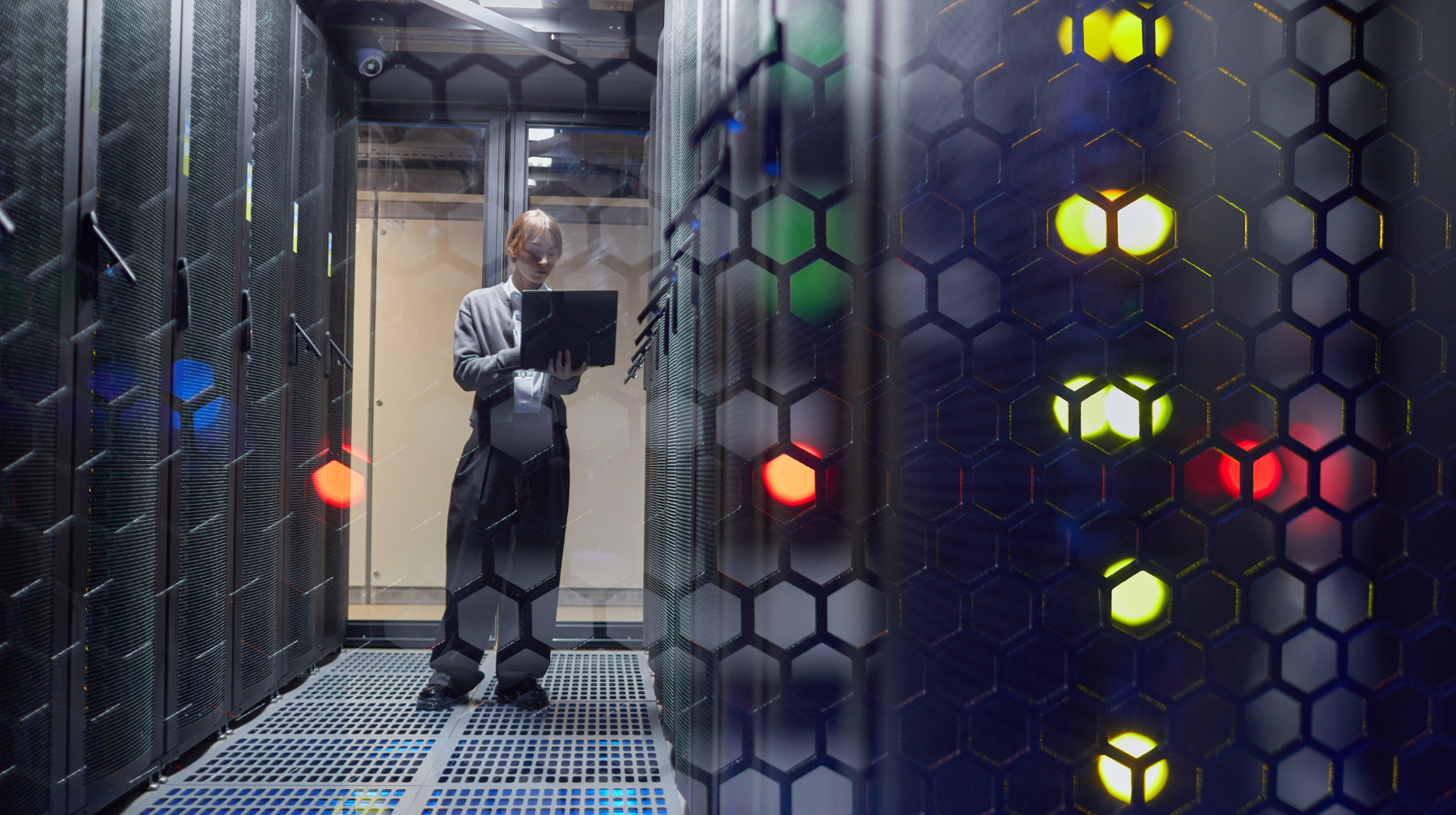 A technician standing between server racks in a data center, working on a laptop.