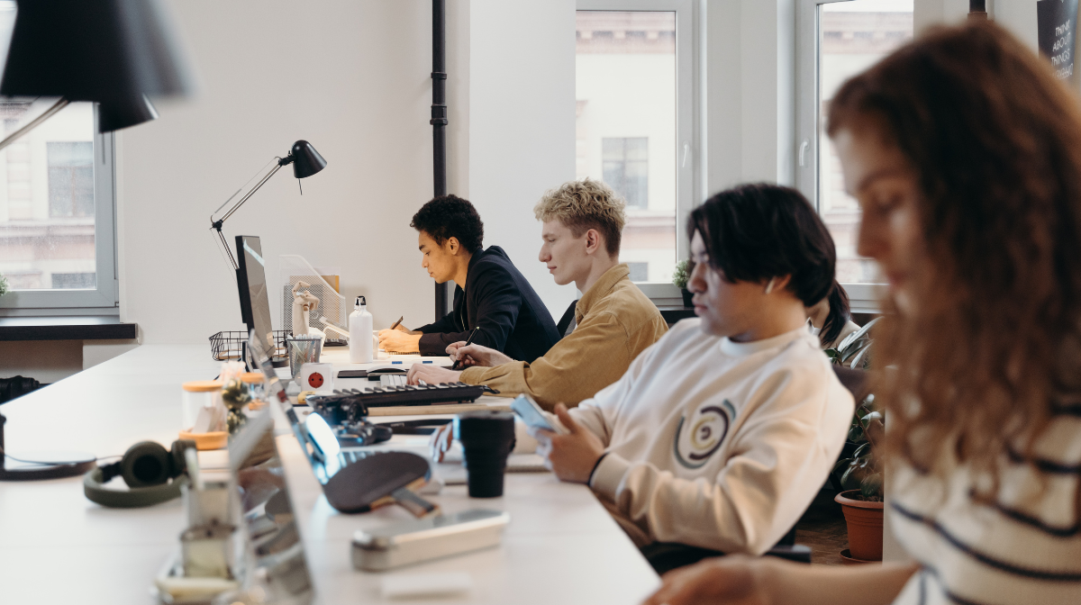 A group of learners working at a shared workspace, each focused on individual tasks on laptops.
