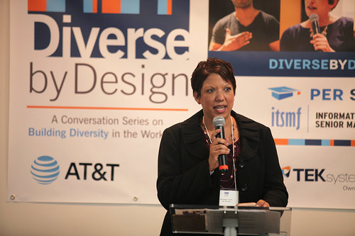 Woman speaking at a podium in front of a "Diverse by Design" banner with sponsor logos.