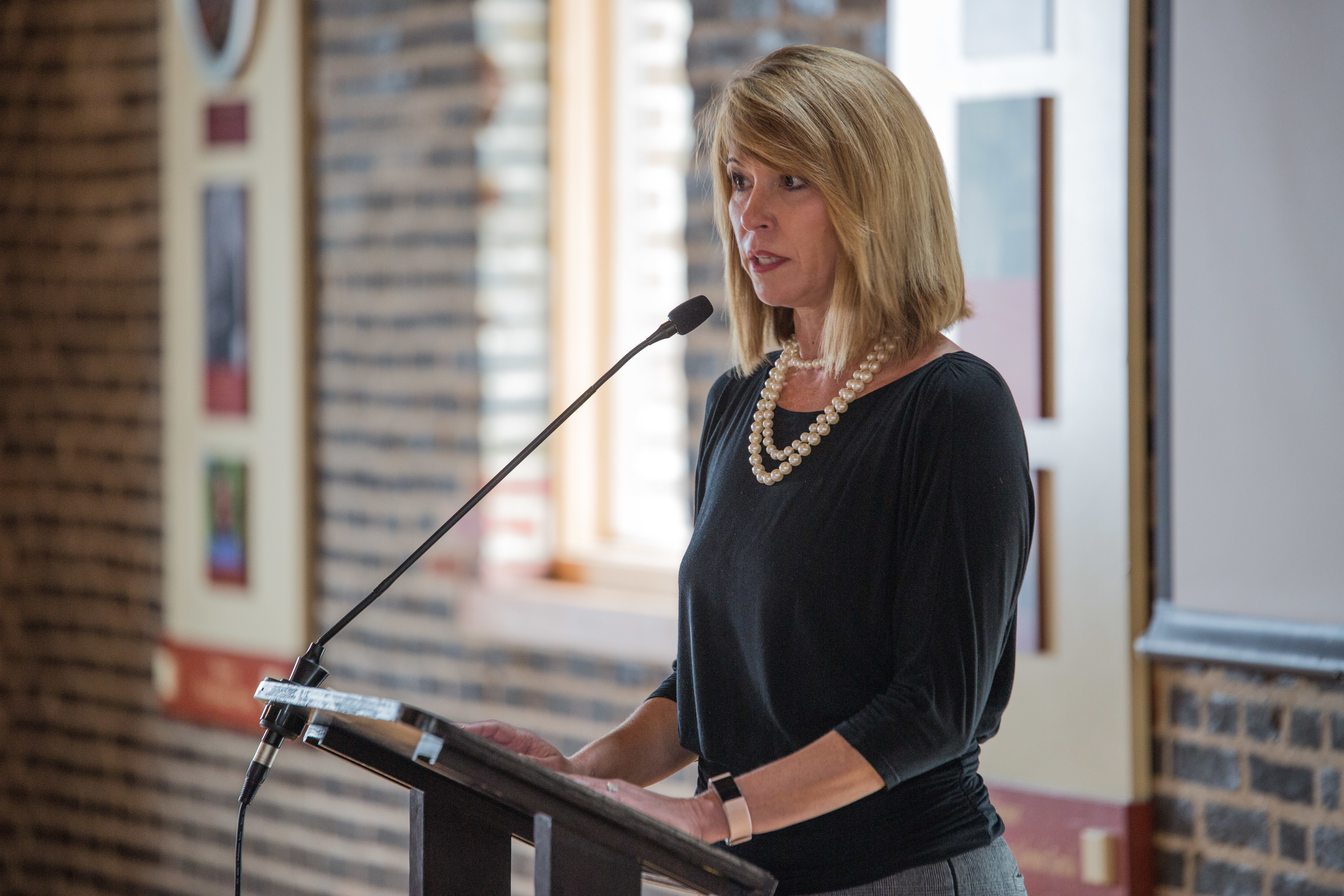 Woman speaking at a podium into a microphone at an indoor event.