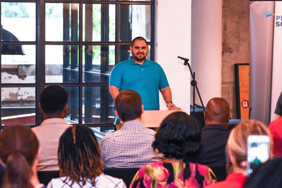 A man stands at a podium speaking to an audience in a event space.