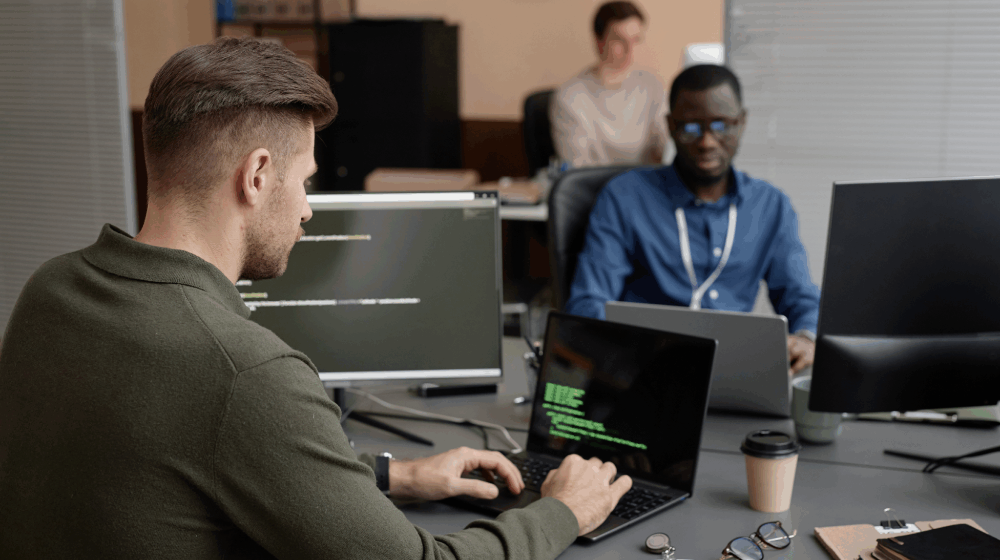 Two young professionals working at laptops in a shared office, focused on coding on their screens.