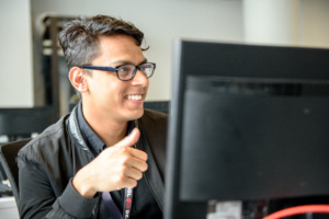 Young adult student at a computer giving a thumbs-up while smiling.