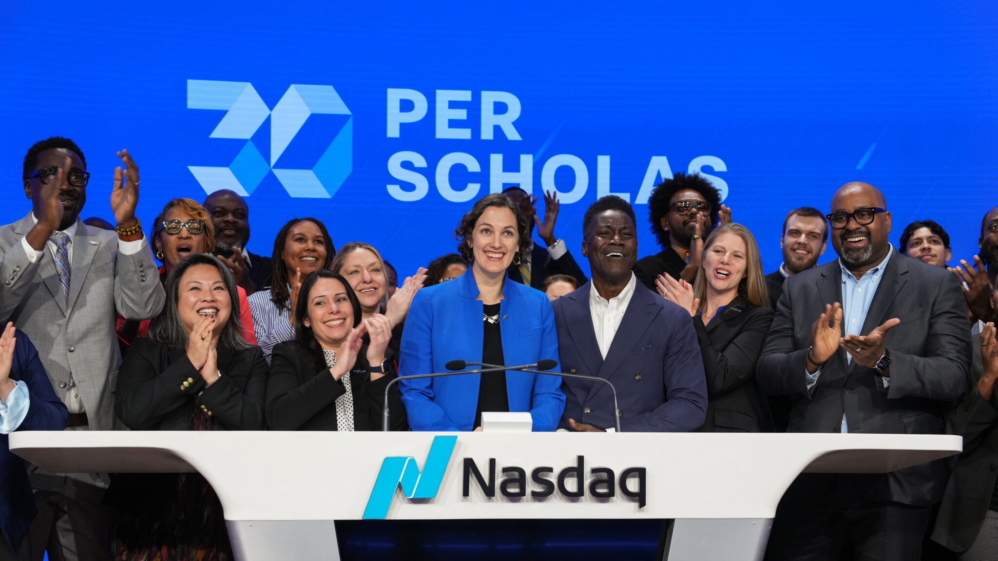 A diverse group of smiling professionals stands behind the Nasdaq podium, celebrating Per Scholas' 30th anniversary.