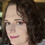 Head-and-shoulders portrait of a young adult with curly hair looking toward the camera with a smile.