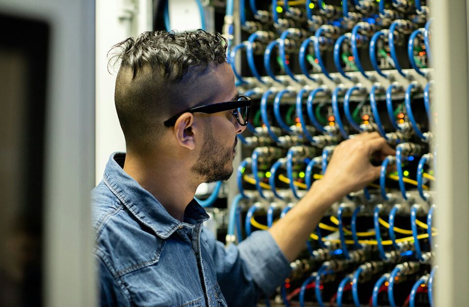Man with glasses closely inspecting and adjusting blue network cables on a server rack in a data center.