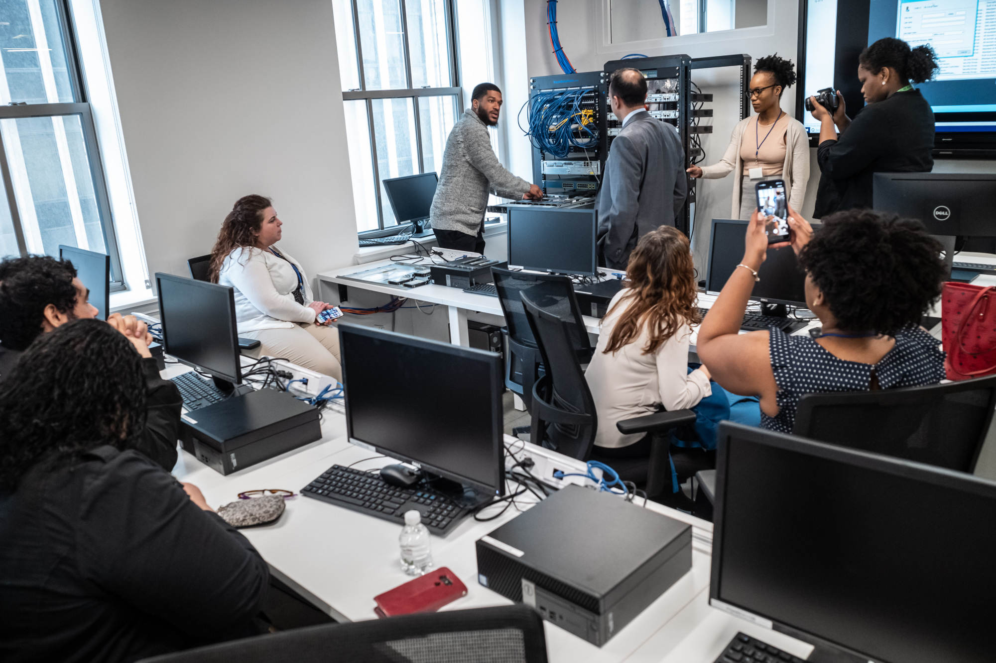 Students and staff gather in a computer lab as an instructor demonstrates networking equipment.