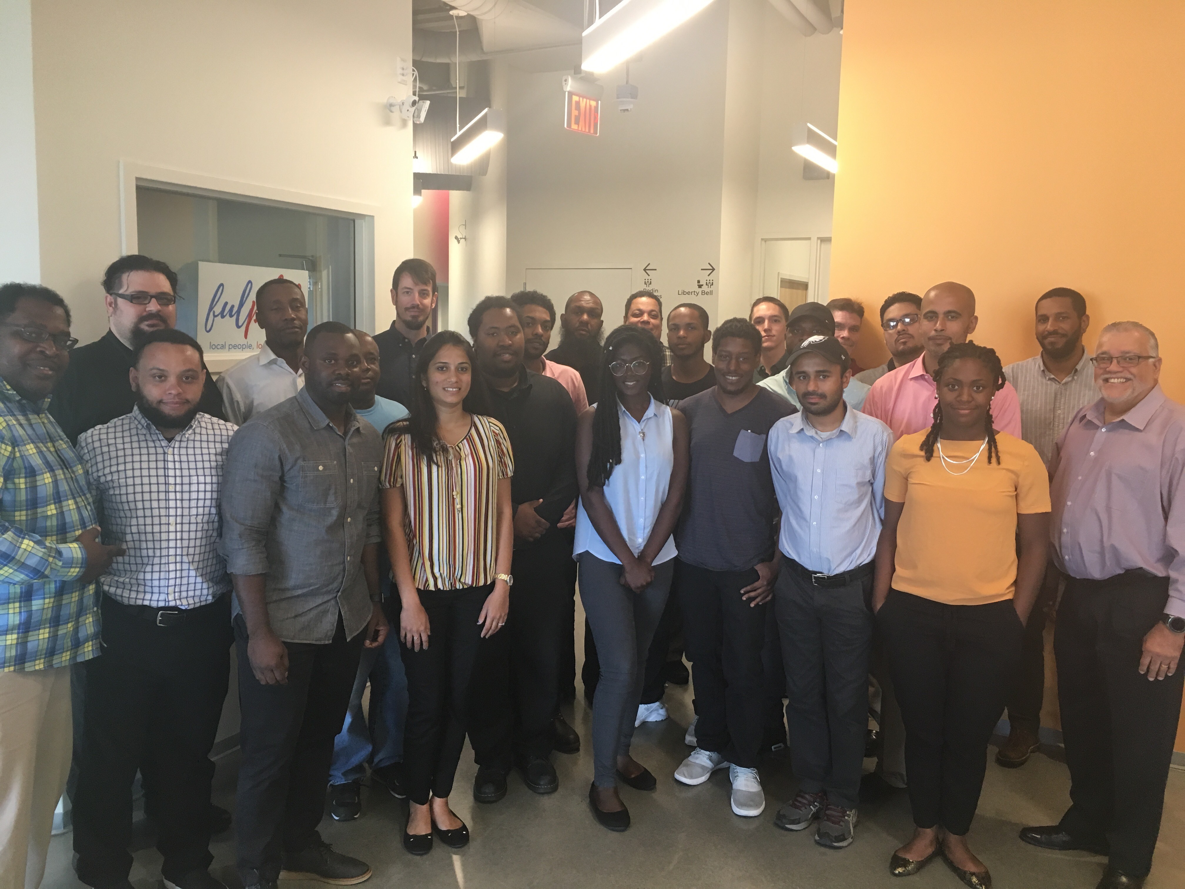 A diverse group of adult students and instructors smiling for a group photo together in a classroom hallway.