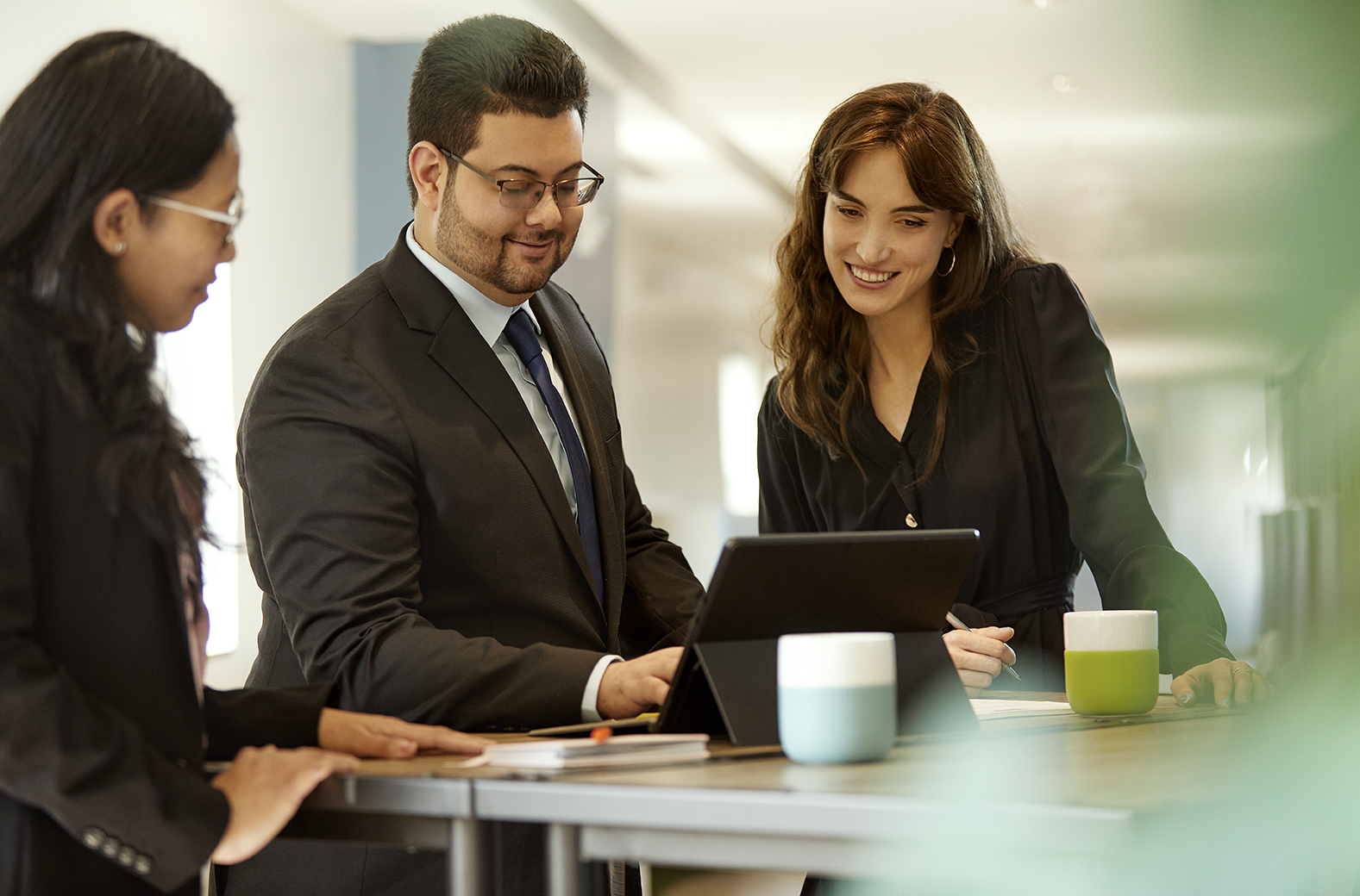 Three professionals gathered around a tablet on a standing desk, collaborating and smiling.