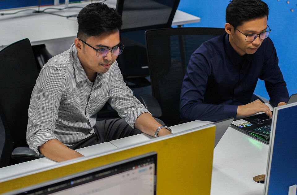 Two coders working on laptops in a classroom environment. 