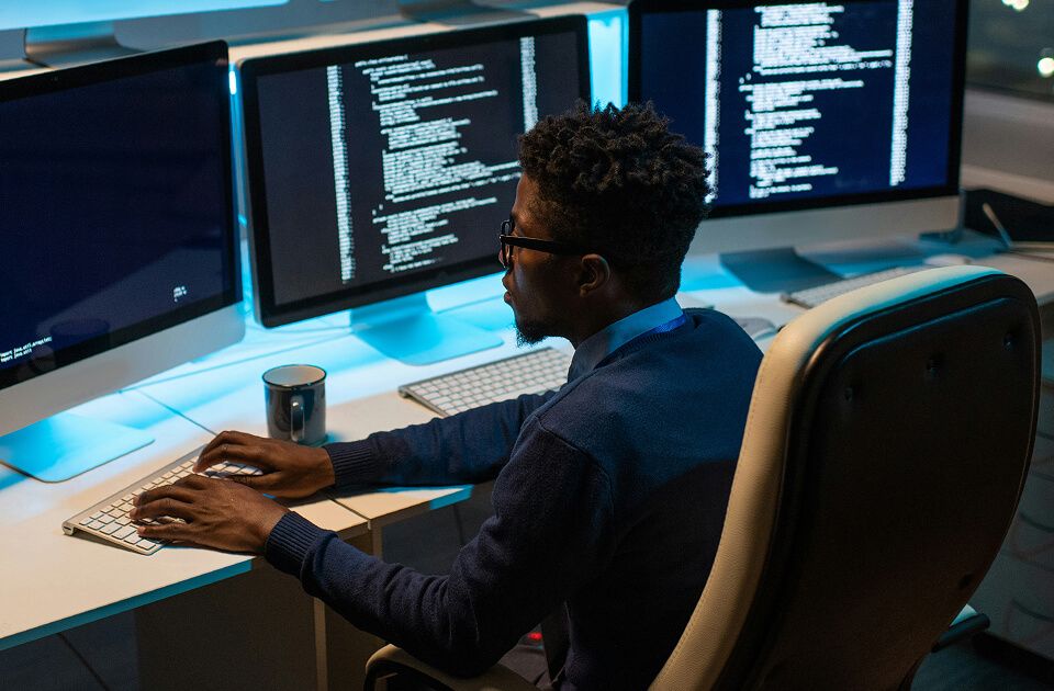 Male professional with glasses working on code across three monitors in an office.