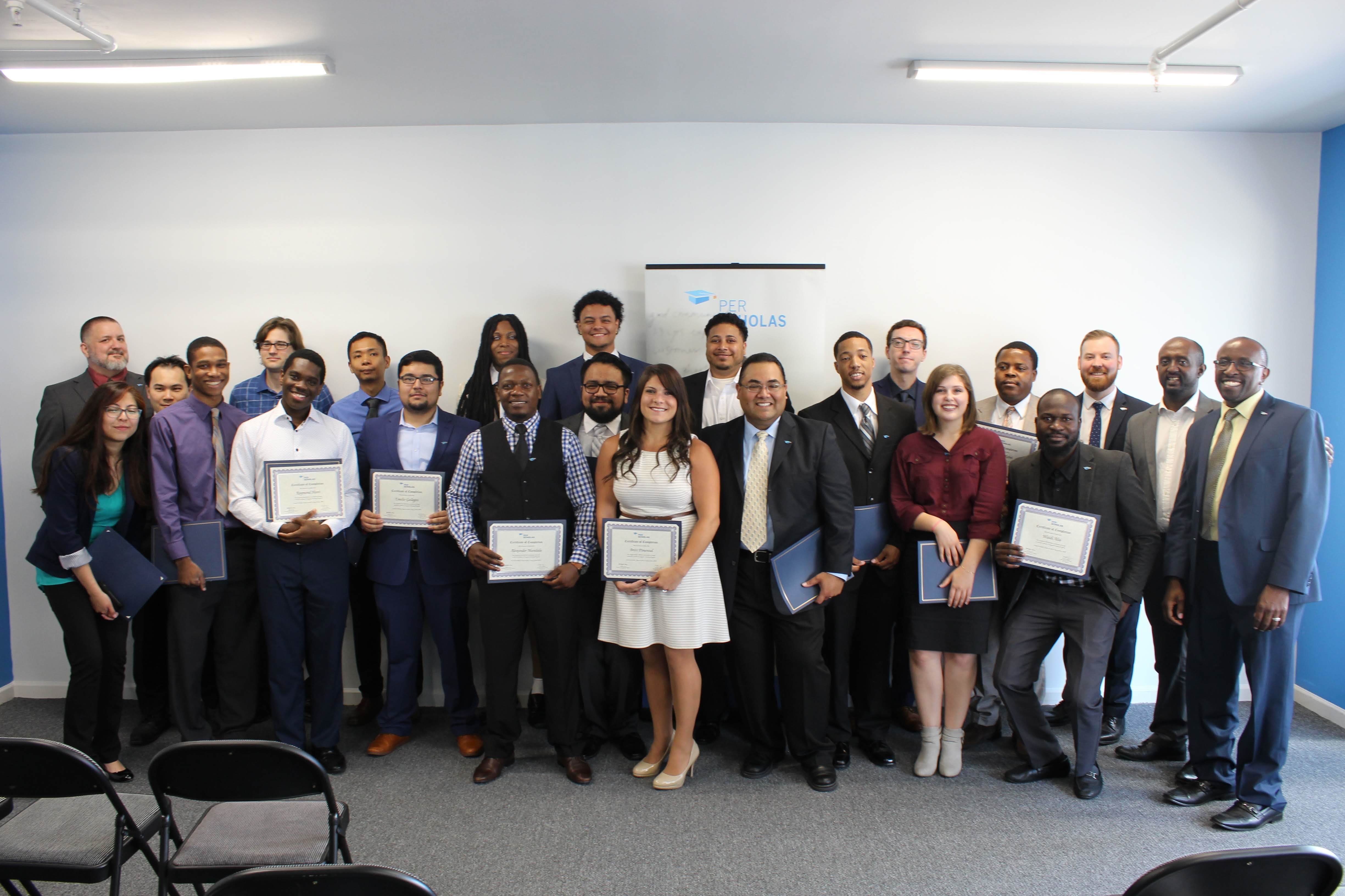 Group of adult graduates holding certificates and folders in a classroom, posing for a photo.