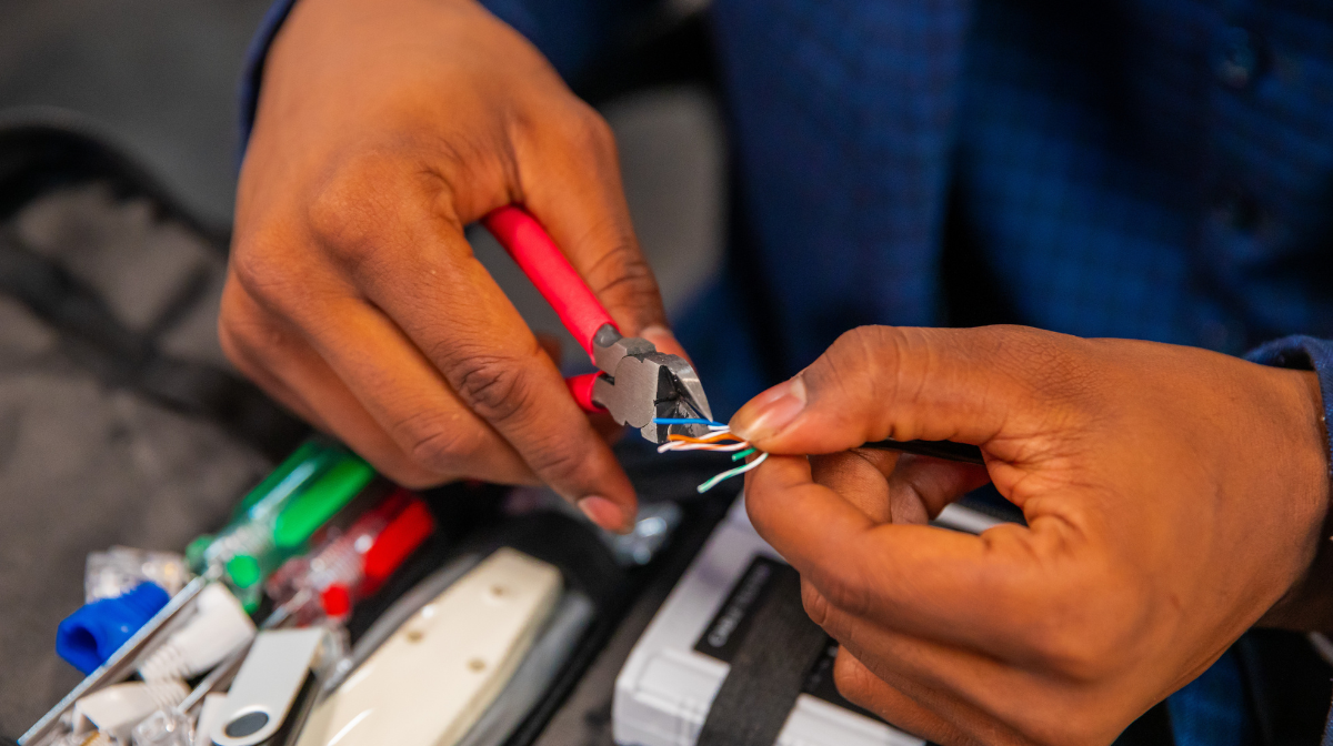 Person using wire cutters to strip and twist the wires of a network cable, with tools and connectors nearby.