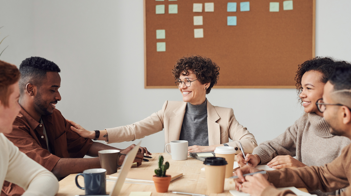 A diverse group of young professionals smiling and collaborating around a conference table.