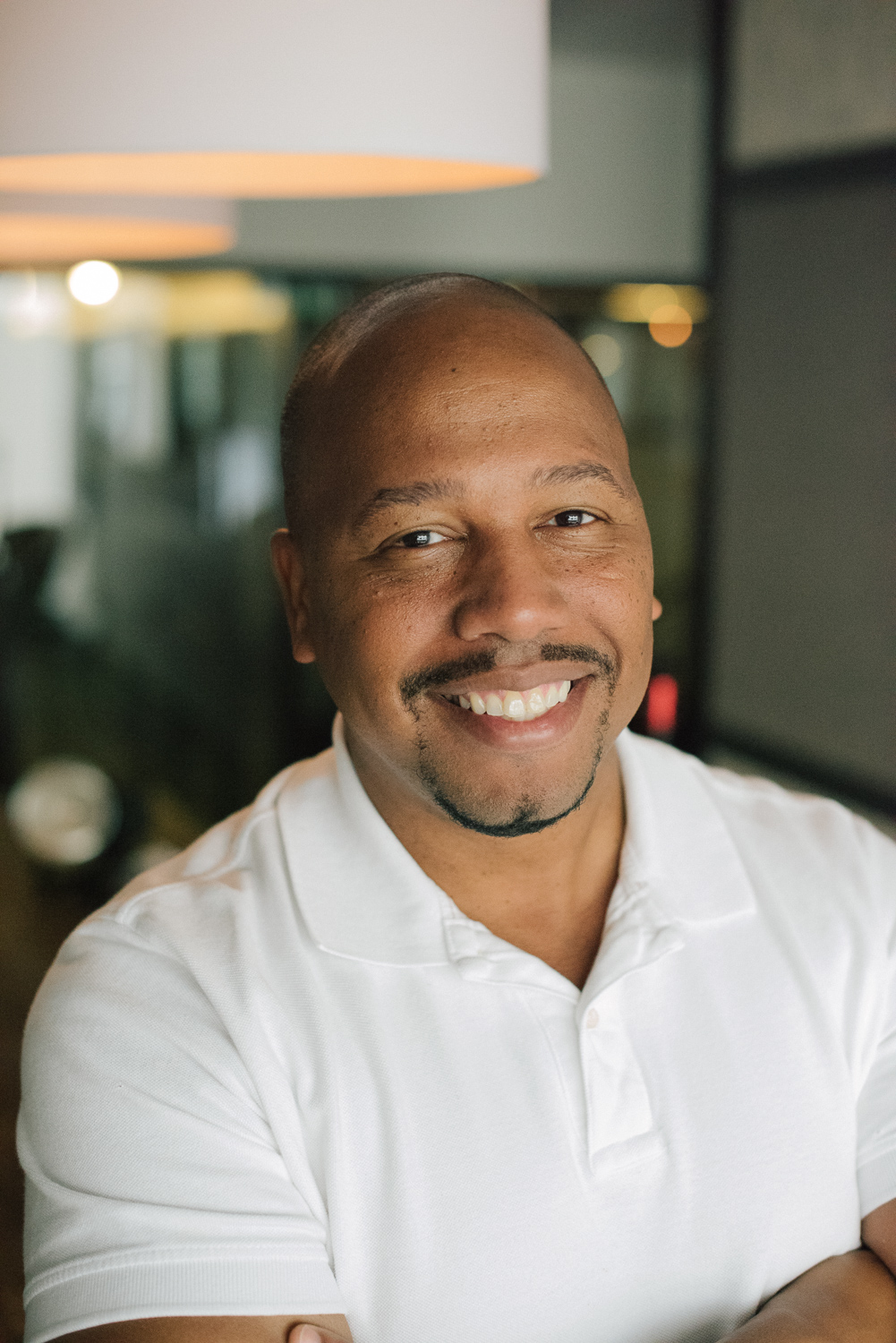 Smiling adult man in a white polo shirt looking at the camera in an indoor workspace.
