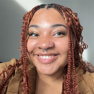Smiling young woman with braided hair and a septum piercing.