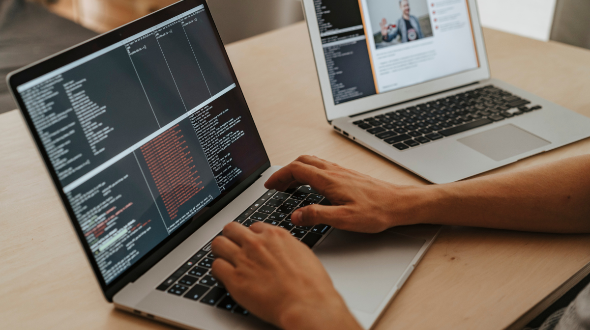 Person typing code on a laptop with another laptop showing a webpage.