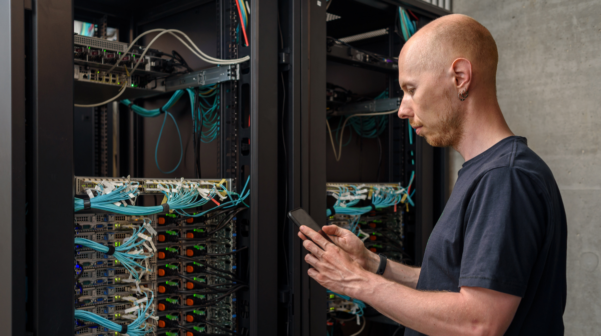 Technician using a smartphone while checking network server racks with organized cabling.