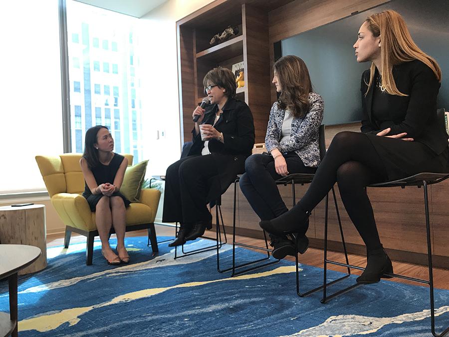 Four women seated in a panel discussion; one woman holds a microphone and speaks while the others listen.