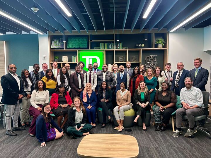 Group of adult learners and professionals smiling in a corporate meeting space in front of a TD logo, posing for a group photo.