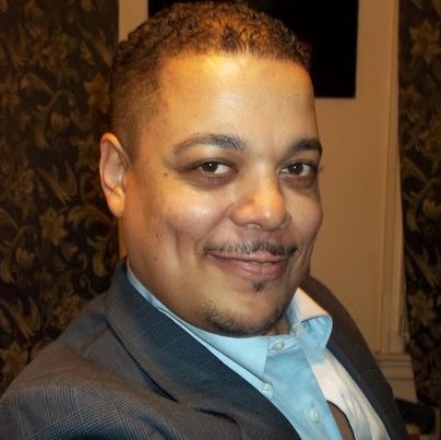 Man smiling at camera in an indoor setting, shown from the shoulders up.