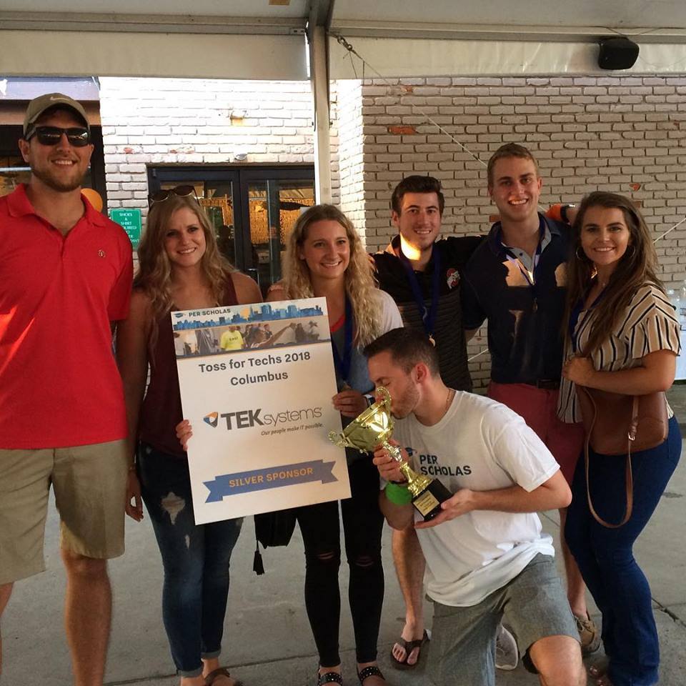 Seven young adults pose under a tent holding a "Toss for Techs 2018 Columbus" sign and a trophy.
